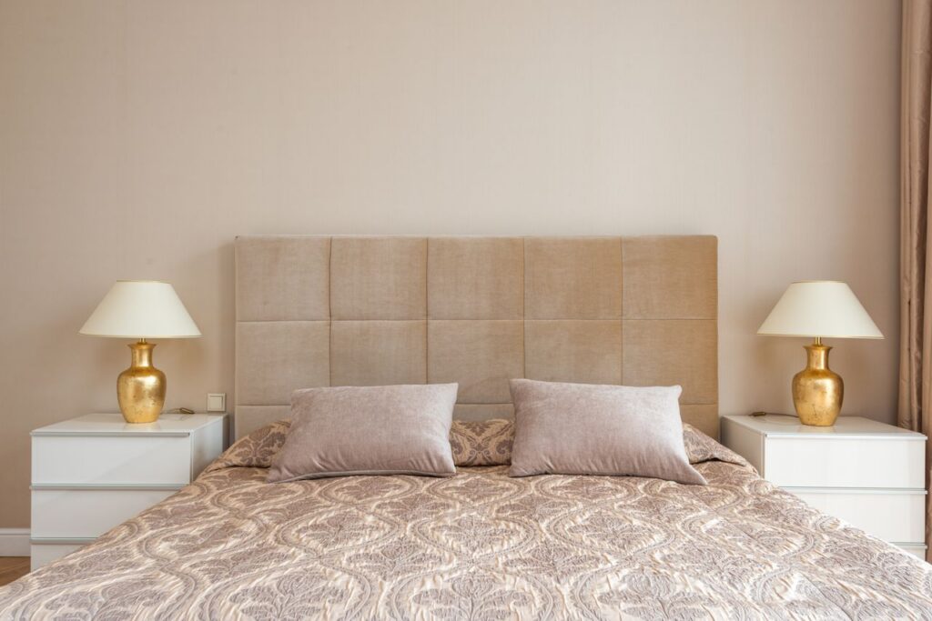 Interior of bedroom with big bed with soft headboard and lamps placed on nightstands in daylight