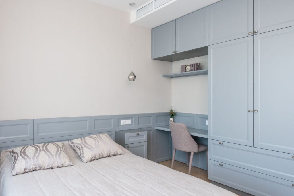 Stylish bedroom features built-in cabinetry, soft blue tones, and a cozy workspace.